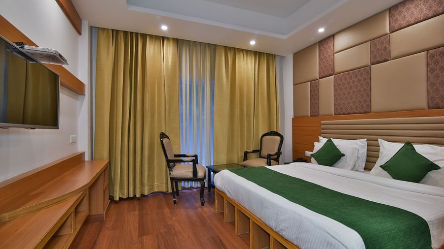 A large bed placed next to two chairs in the Deluxe Room at DLS Highland Resort and Spa, Mussoorie.